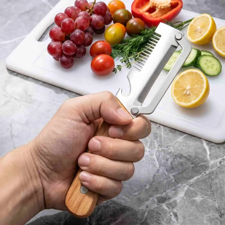 Une main tient l'éplucheur PeelPro au-dessus d'une planche garnie de tomates, de raisins et d'un citron